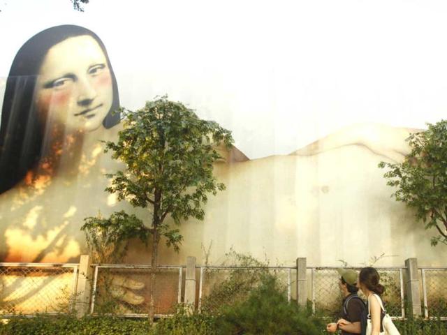 A couple walks past a fence decorated with a painting resembling Mona Lisa in Seoul. The fence was installed to conceal an art museum which was under renovation. (Reuters) 