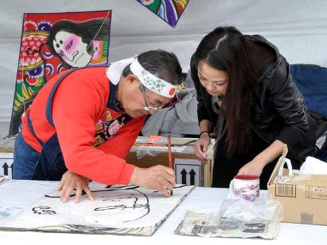 Yoshizo Sakuraba, a member of the Japan Kite Association, demonstrates the art of kite making and painting to a volunteer during the annual Blossom Kite Festival on the National Mall in Wasington, DC. The event is part of the National Cherry Blossom Festival which this year celebrates 100 years of friendship between Japan and the United States. AFP PHOTO/Eva Hambach