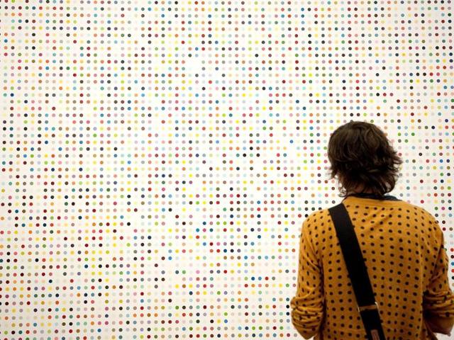 A woman looks at a spot painting by British artist Damien Hirst during the opening of his solo exhibition showcasing work spanning over two decades at the Tate Modern in central London. AFP Photo/Ben Stansall