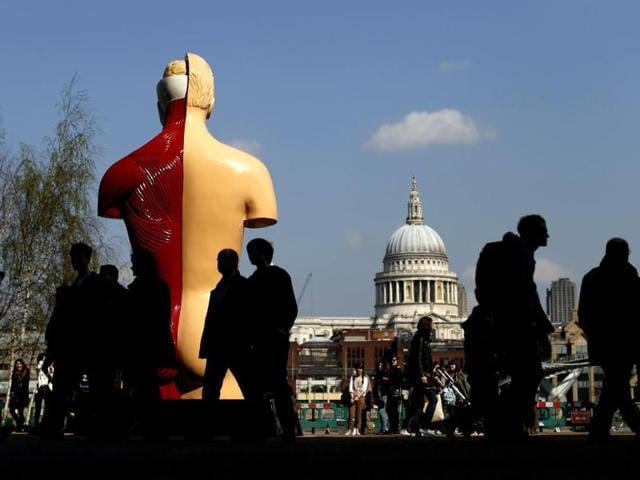 People are silhouetted in the shade as they walk past the back of British artist Damien Hirst's 1999-2005 piece Hymn, a painted bronze, as St Paul's Cathedral can be seen on the other side of the River Thames in the background during a media preview of the first substantial show of his work in the UK at the Tate Modern gallery in London. AP Photo/Matt Dunham