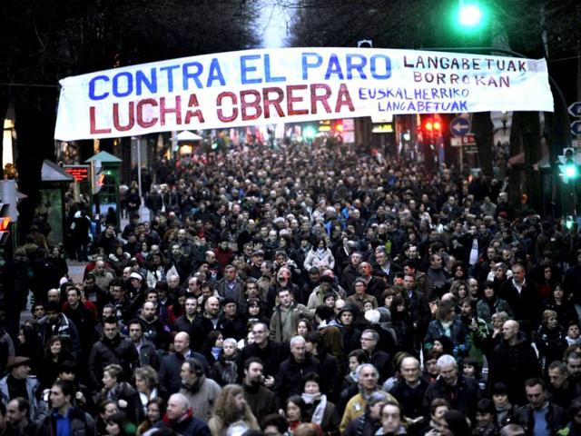 Demonstrators walk under a banner during a protest against cuts in Bilbao. Thousands marched through central Bilbao in protest against unemployment, recent labour reforms and cuts in public and social services. The banner reads "Against Unemployment. Workers Fight". REUTERS/Vincent West