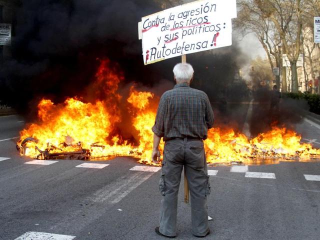 A demonstrator holds a banner in front of a fire started by anti-establishment groups during a general strike in central Barcelona. Spanish workers staged a general strike to protest against labour reforms which the government declared "unstoppable" but many ignored the action, fearing for their jobs in a country with the EU's highest unemployment rate. The words on the banner read "Against the aggression of the rich and their political self-defense". REUTERS/Gustau Nacarino