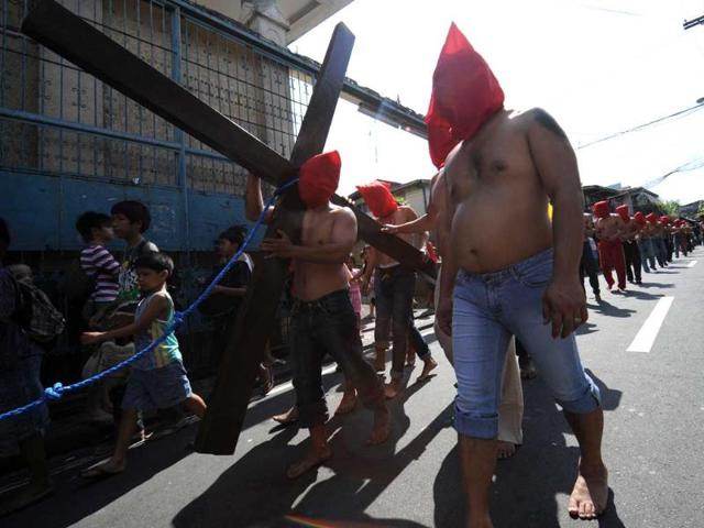 A penitent walking barefoot carries a cross while others flagellates themselves as part of Lenten observance in Manila. AFP Photo/Ted Aljibe