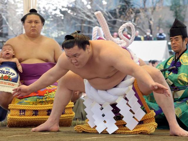 'Yokozuma' or grand champion Hakuho of Mongolia (C) performs a ritual as another wrestler holds his child as they take part in a sumo exhibition at Yasukuni shrine in Tokyo. Sumo wrestlers took part in 'honozumo', a ceremonial one-day exhibition for hundreds of spectators held within the shrine's precincts. AFP/Richard A Brooks