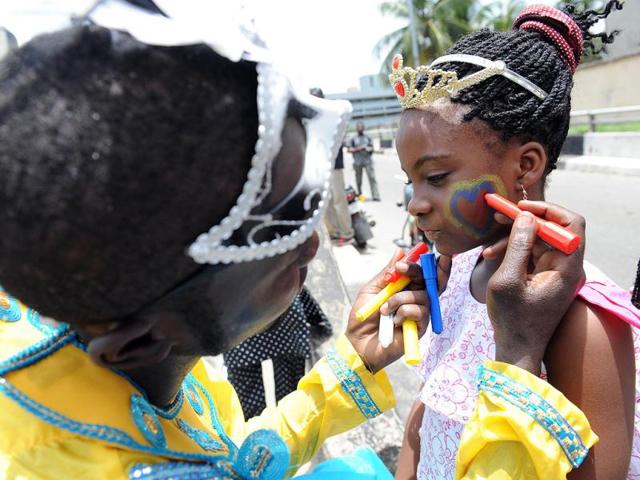 A man paints face of a young girl with the logo of the carnival before a procession during the yearly Lagos carnival. The yearly Lagos carnival to celebrate the Easter festival and the rich cultural heritage of the state was held in Lagos metropolis. AFP PHOTO / PIUS UTOMI EKPEI