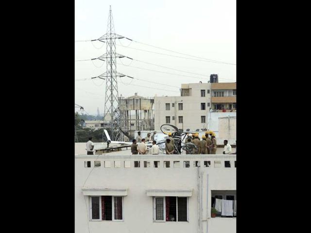 Police and fire department personnel, including Hindustan Aeronautics Limited officials, at dusk near a Schweizer helicopter that made an emergency landing on the rooftop of a residential building in Bangalore. (AFP Photo)