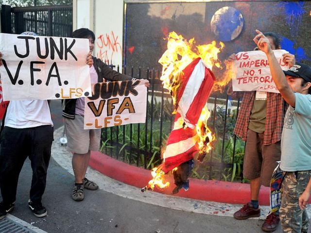 Students burn a US flag after vandalising the outer wall of the US embassy, during a lightning protest in Manila. (AFP Photo/Noel Celis)