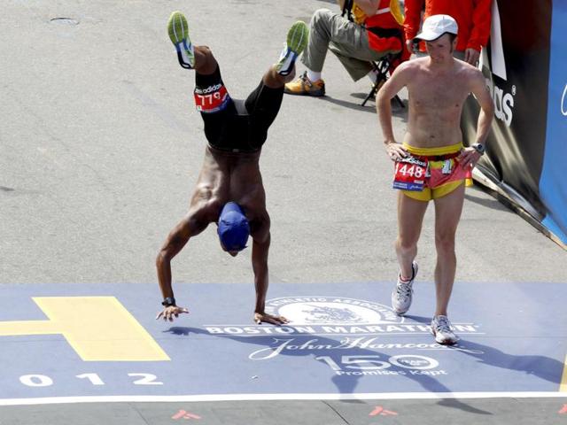 Jeremy Doody (R) watches as Remus Medley (L) walks on his hands across the finish line of the 116th Boston Marathon after his legs cramped up in Boston, Massachusetts. (Reuters/Jessica Rinaldi)