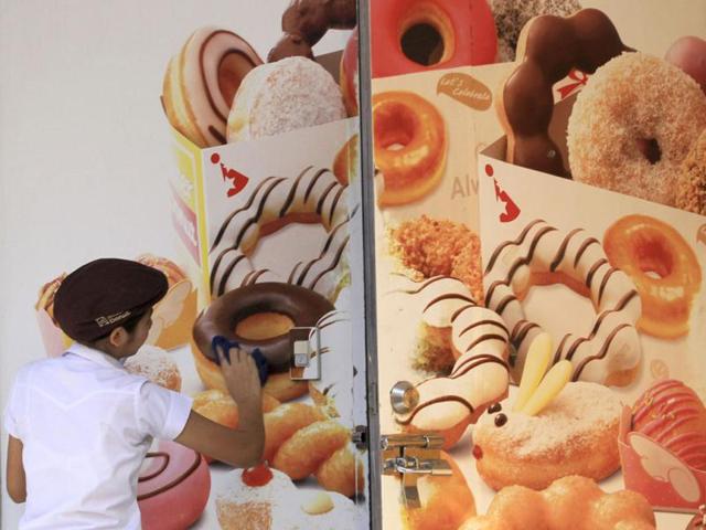 A worker cleans an advertising banner at a doughnut shop in Bangkok ,Thailand.(AP Photo/Sakchai Lalit)