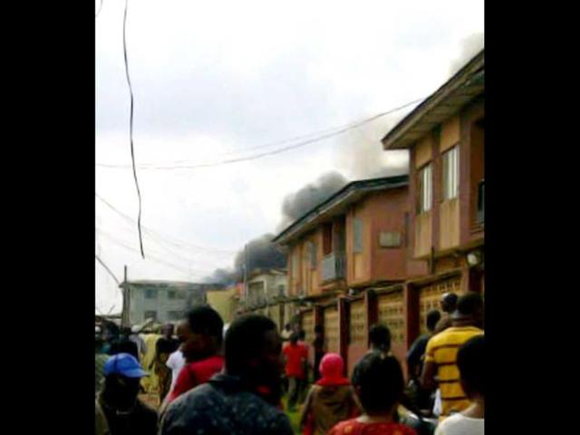 A picuture taken with a photo camera shows residents of the Iju district of Lagos looking at the smoke that rises a few moments after a Dana company aircraft crashed into a two-storey building on June 3, 2012 in Lagos. More than 150 passengers are feared dead, an aviation official and residents said. Thick smoke rose from the area near the Lagos airport and flames could be seen coming from the building. Residents said the plane had been coming in low, making a loud noise, when it slammed into the residential area. AFP PHOTO / CKN