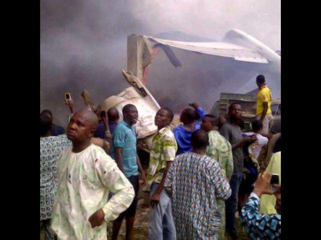 A picture taken with a photo camera shows residents of the Iju district of Lagos gathering at the site where a Dana company aircraft crashed into a two-storey building on June 3, 2012 in Lagos. More than 150 passengers are feared dead, an aviation official and residents said. Thick smoke rose from the area near the Lagos airport and flames could be seen coming from the building. Residents said the plane had been coming in low, making a loud noise, when it slammed into the residential area. AFP PHOTO / CKN