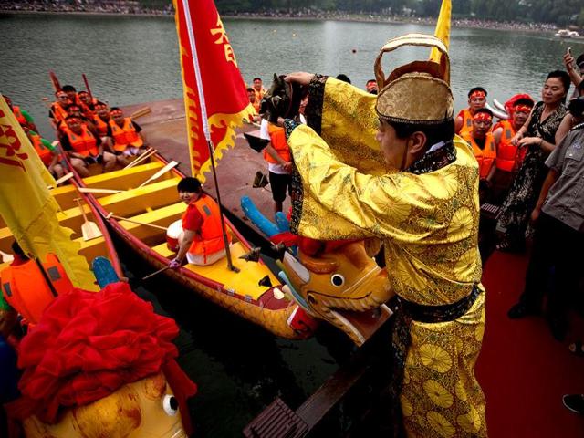 A Chinese actor dressed in an emperor costume pours rice dumplings near the dragon boats during a religious ritual to honor Chinese poet Qu Yuan during the Duanwu Festival at Longtan park in Beijing, China. Rice dumplings are traditionally eaten during the Duanwu festival, also known as the Dragon Boat festival, which falls on the fifth day of the fifth month of the Chinese calendar, commemorating the death of Qu Yuan, a famous Chinese poet from the kingdom of Chu who lived during the Warring States period. (AP Photo/Andy Wong)