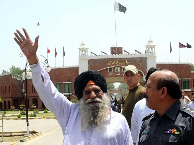 Freed Indian prisoner Surjeet Singh, escorted by Pakistani security officials, waves before leaving Pakistan for India at the Wagah border. AFP/Arif Ali