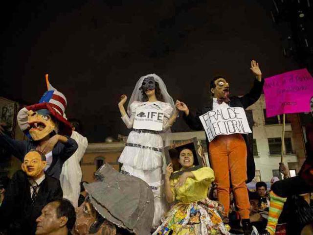 Members of the Mexican university student movement I Am #132 perform in front of anti-riot policemen standing guard at the entrance of the national TV network TELEVISA during a protest against presidential candidate of the Institutional Revolutionary Party (PRI), Enrique Pena Nieto in Mexico City the day before presidential elections. AFP/Yuri Cortez