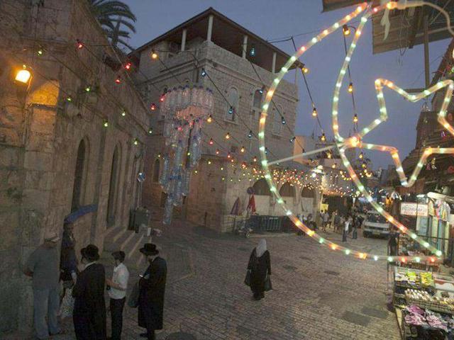 A Palestinian woman walks as Israeli Ultra-Orthodox Jewish men stand in a street decorated with Ramadan decorations, in the old city of Jerusalem to welcome the upcoming Muslim holy fasting month of Ramadan.(AFP Photo/Ahmad Gharabli)
