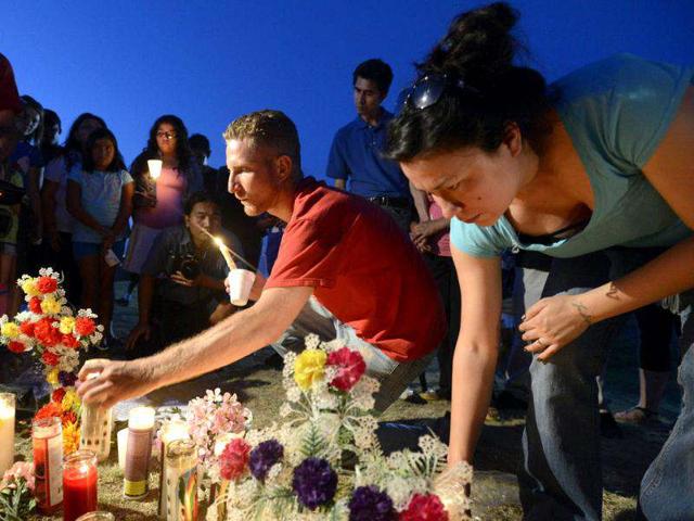 Justin Konye (C) places candles with other mourners during a vigil for victims behind a theater where a gunman open fire at moviegoers in Aurora, Colorado. (Reuters/ Jeremy Papasso)