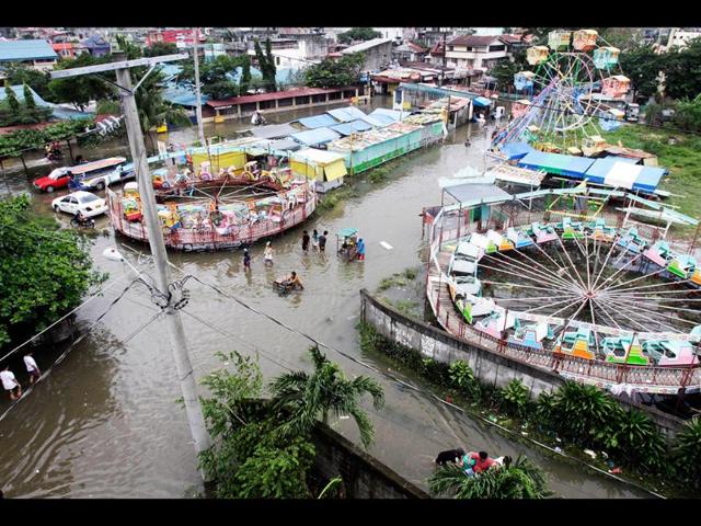 Local residents continue with their daily activities as the village carnival remains out of operation as the area is submerged in flood water in Taytay town east of Manila, Philippines. AP/Pat Roque