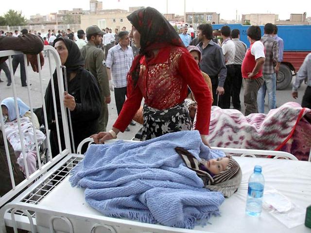 An Iranian woman stands next to her injured child lying on a bed outside a hospital in the town of Ahar, some 60km east of Tabriz, after a strong earthquake hit northwestern Iran. AFP/Kamel Rouhi