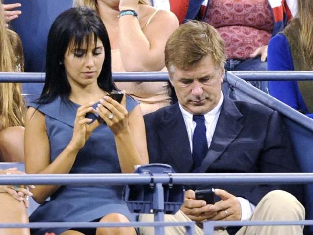 Actor Alex Baldwin (R) and wife Hilaria Thomas work on their phones as they attend the opening night matches at the US Open tennis tournament in New York. (Reuters/Bill Kostroun)
