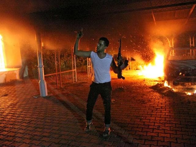 An armed man waves his rifle as buildings and cars are engulfed in flames after being set on fire inside the US consulate compound in Benghazi. AFP