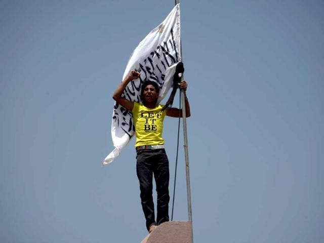 A Yemeni protester holds a flag bearing Islamic calligraphy as he stands above the gate of the US embassy in Sanaa during a protest over a film mocking Islam. Yemeni forces managed to drive out angry protesters who stormed the embassy in the Yemeni capital with police firing warning shots to disperse thousands of people as they approached the main gate of the mission. AFP PHOTO/MOHAMMED HUWAIS