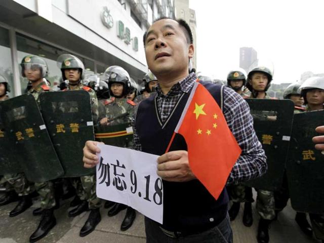 A protester holds a Chinese national flag and a paper bearing slogan as he stands in front of paramilitary policemen on the 81st anniversary of Japan's invasion of China, in Chengdu, Sichuan province. (Reuters)