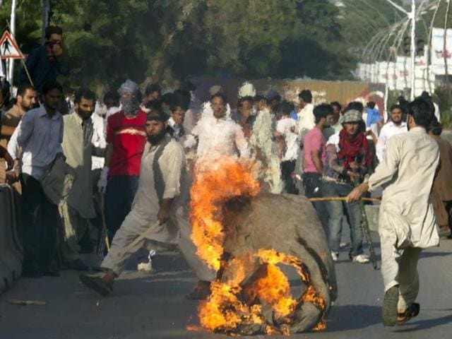 A Pakistani protester carries a burning piece of canvas towards containers police had placed to block the road leads to the diplomatic enclave in Islamabad. AP Photo/BK Bangash