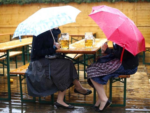 Revellers sit under umbrellas with their traditional one-litre "Masskrug" beer mugs on a beer garden table during heavy rain falls at the opening day of the Munich Oktoberfest at the Theresienwiese in Munich. REUTERS/Kai Pfaffenbach