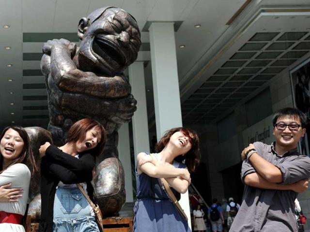 Mainland tourists pose for a photograph next to a sculpture by Chinese born artist Yue Minjun during an outdoor exhibition in Hong Kong. Yue Minjun is a contemporary Chinese artist based in Beijing and is best known for oil paintings depicting himself in various settings like "frozen in laughter." AFP Photo
