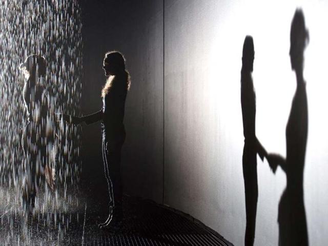 Two women shake hands as they pose for pictures in an art installation entitled "Rain Room" during a photocall at the Barbican in London. AFP/Leon Neal