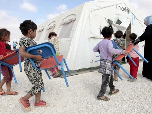 Young Syrian refugees carry their chairs into a classroom at a UNICEF-run school in the al-Zaatari refugee camp in the Jordanian city of Mafraq near the border with Syria. The school is a grant from the European Union to provide education to Syrian refugees residing in Jordan. AFP/Khalil Mazraawi