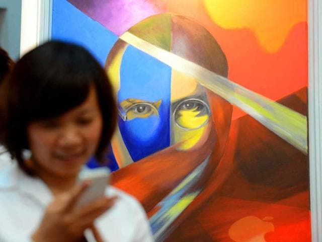 A woman uses an Iphone next to a portrait of Steve Jobs at an art exhibition in commemoration of the late Apple's co-founder Steve Jobs on the occasion of his first death anniversary in Hanoi. AFP Photo/Hoang Dinh Nam