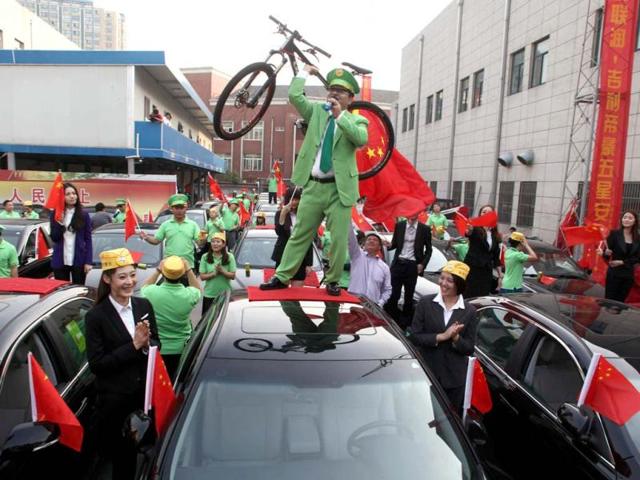Chen Guangbiao, dressed in green, holds up a bicycle as he stands on a car in Nanjing, Jiangsu province. Chen, a Chinese entrepreneur, bought 43 Geely cars to compensate people whose Japanese-brand cars had been damaged during a series of anti-Japan protests throughout China last month. Reuters Photo