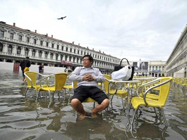 A tourist sits outside a cafe in flooded St. Mark square as high tides reached 1.05 meters above sea level, partly flooding the city of Venice. AP photo