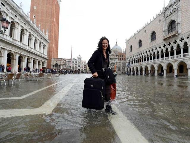 A tourist carries a suitcase as she walks barefoot on a flooded St Mark's square during the first "acqua alta" of the season in Venice. The "acqua alta", a convergence of high tides and a strong sirocco, reached 105 centimeters. AFP photo