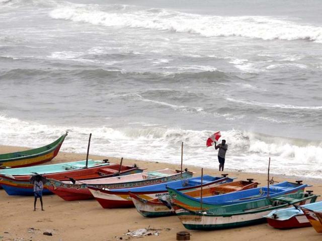 A man tries to hold on to his umbrella in strong winds, as he stands beside fishing boats on the Bay of Bengal coast as tidal waves approach the shore in Chennai. AP Photo