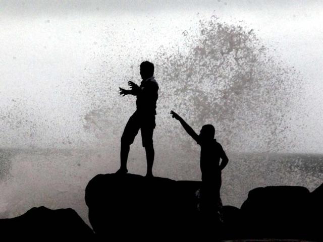 Boys play as waves strike the promenade at the fishing harbour in Chennai. PTI Photo