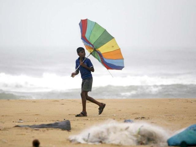 A boy tries to hold his umbrella against strong winds as he walks the Bay of Bengal coast in Chennai. AP Photo