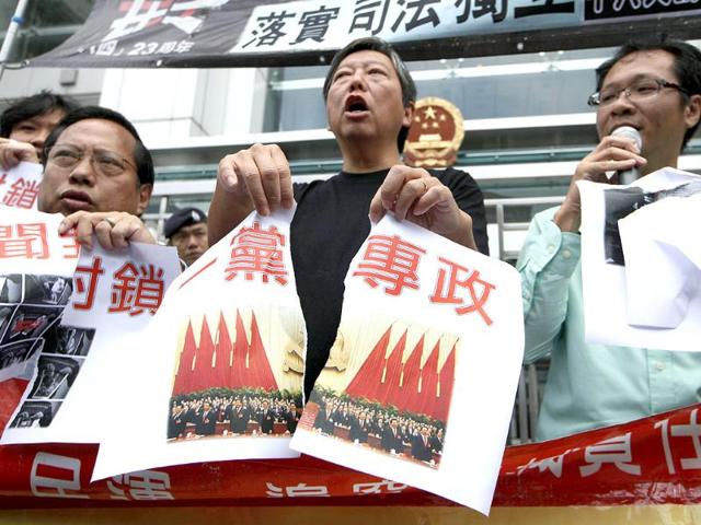 Pro-democracy activists tear a picture of the 18th Communist Party Congress held in Beijing with Chinese writing reading "One party rule in China" outside the Chinese central government's liaison office in Hong Kong. (AP Photo/Kin Cheung)