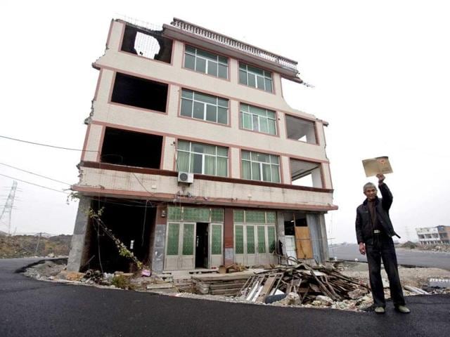 In-this-file-photo-Luo-Baogen-shows-his-land-certificate-as-he-stands-next-to-his-house-sitting-in-the-middle-of-a-new-main-road-on-the-outskirts-of-Wenling-city-in-east-China-s-Zhejiang-province-AP-Photo-File In-this-file-photo-Luo-Baogen-shows-his-land-certificate-as-he-stands-next-to-his-house-sitting-in-the-middle-of-a-new-main-road-on-the-outskirts-of-Wenling-city-in-east-China-s-Zhejiang-province-AP-Photo-File