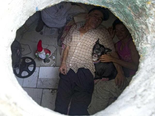 Colombian Miguel Restrepo, rests with his wife Maria Garcia and their dog on a bed inside a sewer in Medellin, Antioquia department, Colombia. The place is around three by two by 1.4 meters of height and has a stove, a television, a bed and a fan. AFP Photo