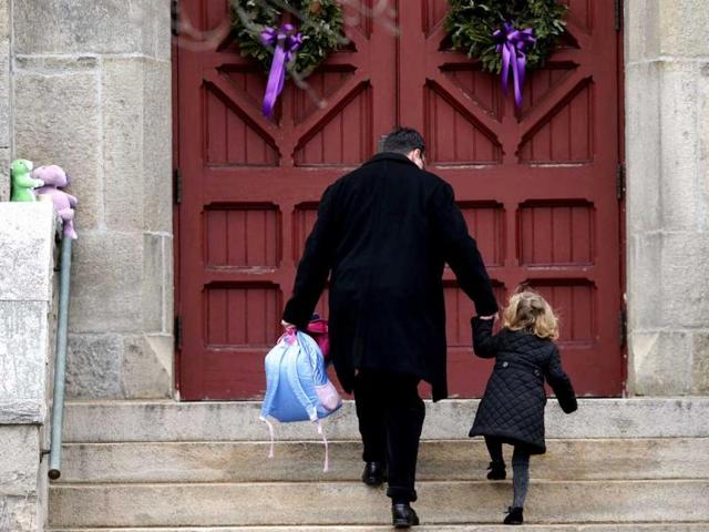 A man helps a young girl up the stairs while carrying her backpack as they arrive for services at Trinity Church in Newtown, Connecticut. A gunman walked into Sandy Hook Elementary School in Newtown Friday and opened fire, killing 26 people, including 20 children. AP photo