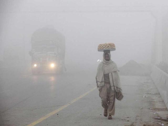 A biscuit street seller walks along the highway amid dense fog on a cold morning in Lahore. Reuters