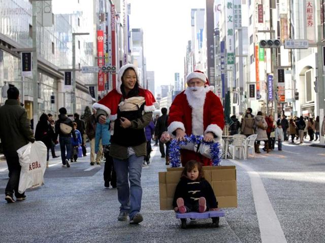 Second Harvest Japan executive director Charles McJilton dressed as Santa Claus, accompanied by his wife and son pushes a cart after handing out picture books attached with donation envelops to passersby on the main street of Tokyo's Ginza shopping district. Second Harvest is one of the largest non-profit food banks based in the United States for the needy people. (AP Photo)