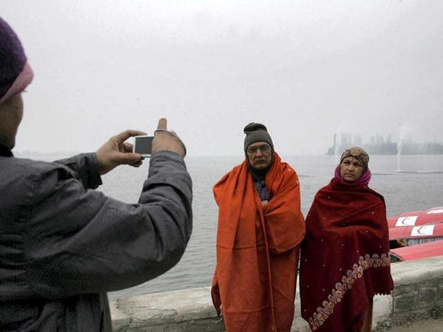 A tourist clicks photograph of his parents on the banks of Dal Lake during a cold day in Srinagar. (PTI Photo)