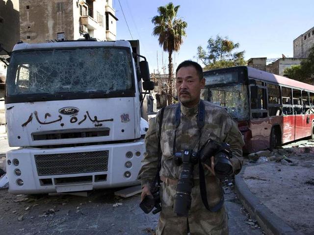 Japanese-trucker-Toshifumi-Fujimoto-holds-his-cameras-in-front-of-damaged-buses-in-Aleppo-s-old-city-on-December-27-2012-Photo-AFP-STR Japanese-trucker-Toshifumi-Fujimoto-holds-his-cameras-in-front-of-damaged-buses-in-Aleppo-s-old-city-on-December-27-2012-Photo-AFP-STR