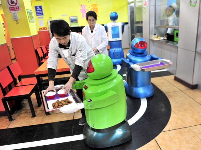 A robot that specialises in delivering food holds a tray as a waiter puts dishes on it at a Robot Restaurant in Harbin. Reuters