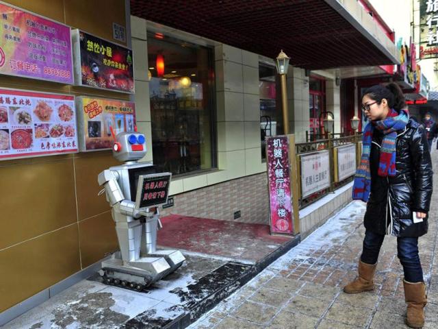 A pedestrian looks at a robot that specialises in greeting people outside a Robot Restaurant in Harbin, Heilongjiang province. The sign the robot is holding reads, "Robot Restaurant, go downstairs and have dinner." Reuters Photo