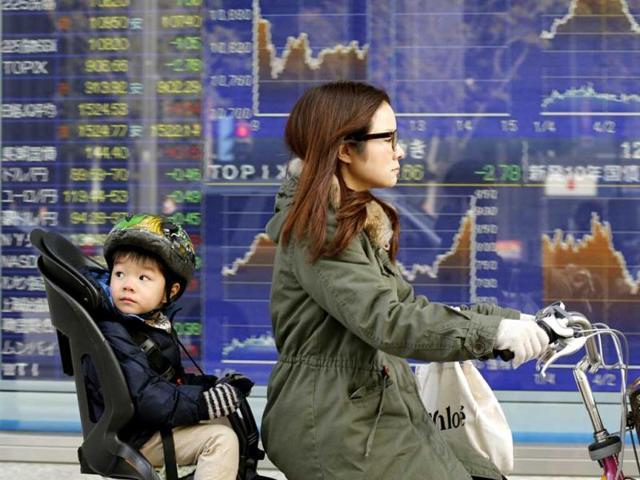 A mother and child cycle past an electronic stock board of a securities firm in Tokyo. Asian stock markets were mixed Monday amid uncertainty about the outcome of a central bank meeting in Japan and nervousness over whether US political leaders will be able to reach a deal on the government's debt limit. AP Photo