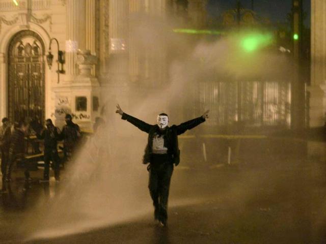 A protestor wearing a Guy Fawkes mask, trademark of the anonymous movement and based on a character in the film V for Vendetta, is sprayed by water as Egyptian security use water cannons to disperse anti-government protestors as they throw stones into the grounds of the al-Kobaa Presidential palace in Cairo. (AFP Photo)